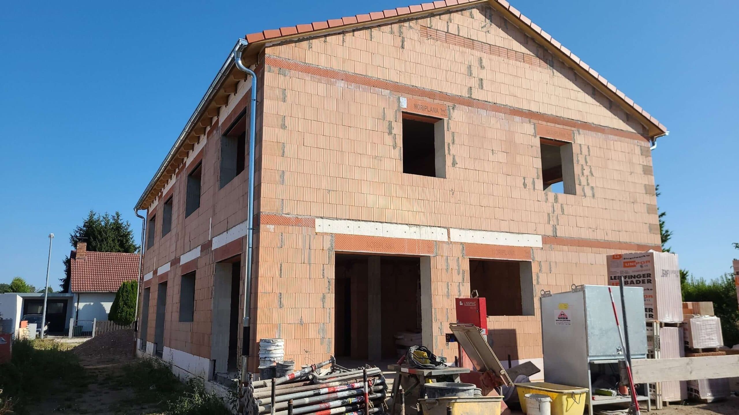 Ein unvollständiges zweistöckiges Haus aus Ziegelstein mit Baugeräten und Baumaterialien im Vordergrund.