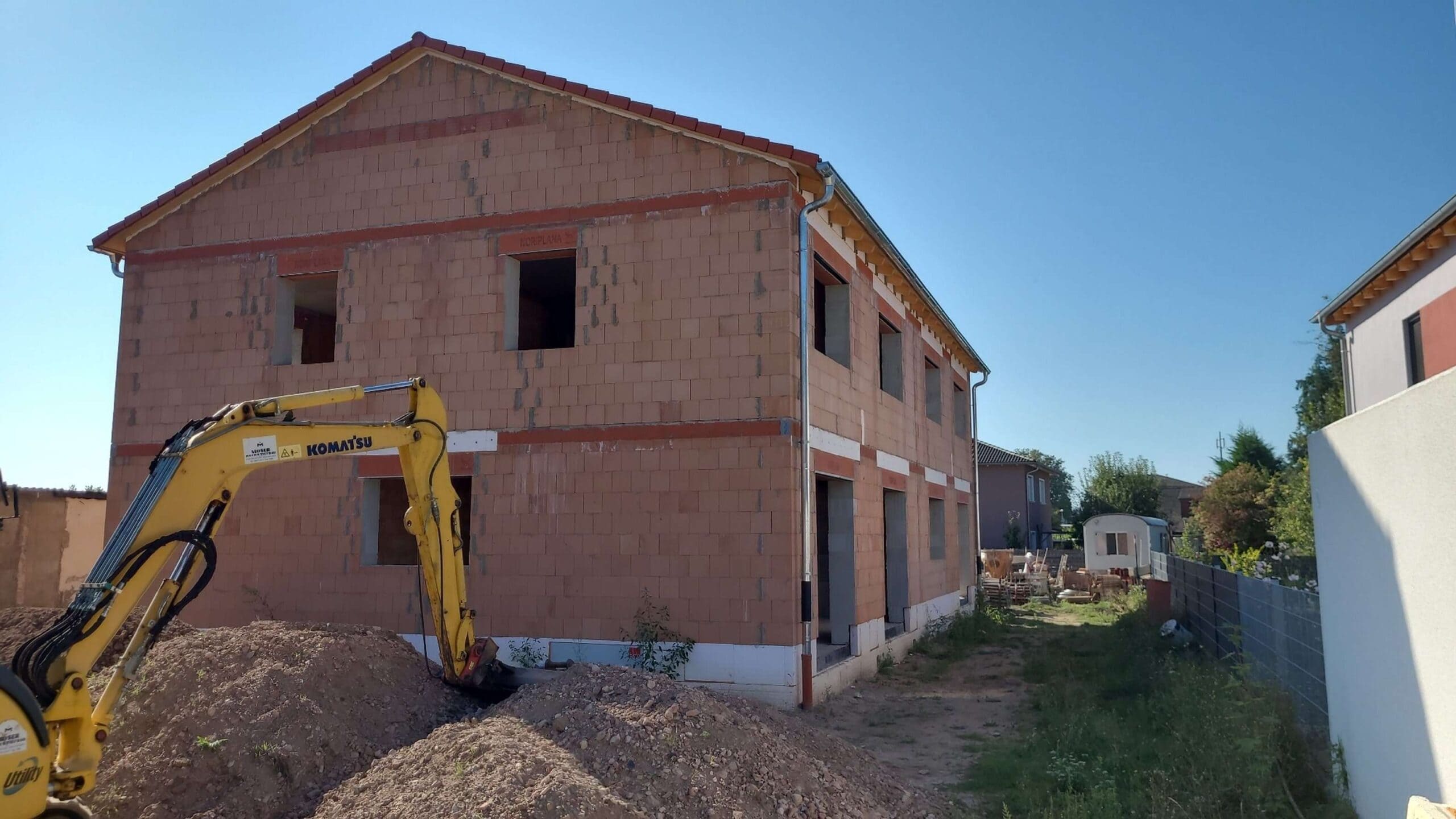 Eine unfertige braune Mauerhausstruktur mit gelbem Bagger bei sonnigem Wetter.