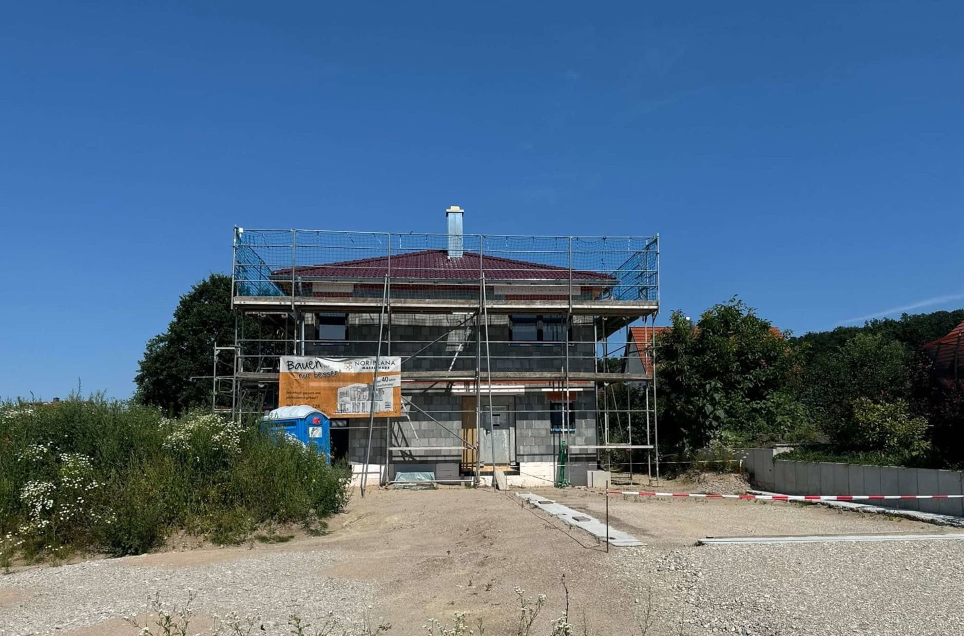 Eine Baustelle mit einem zweistöckigen Haus in Gelb; Gerüst um das Haus; blauer Himmel im Hintergrund.